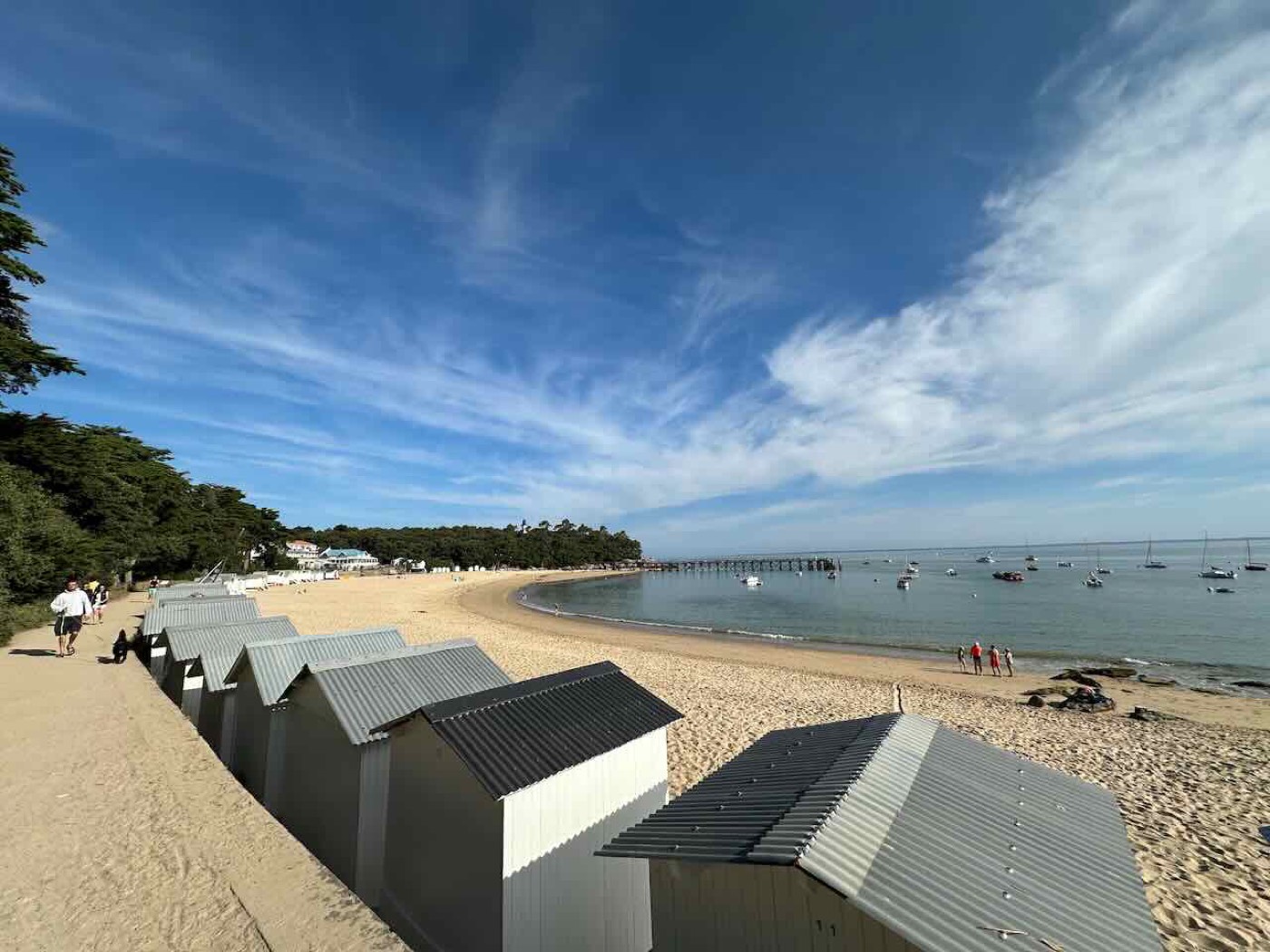 The white beach huts and pier at Plages des Dames on a bright day